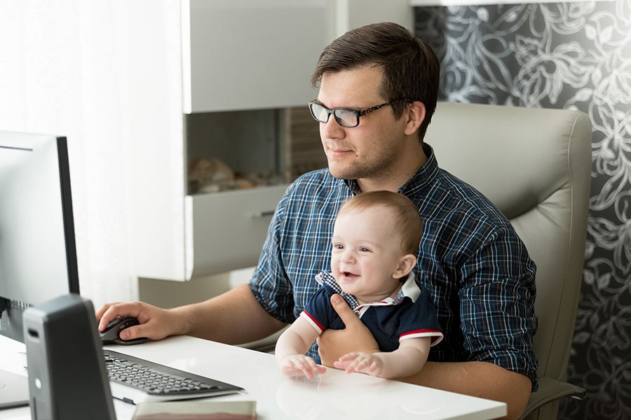 A father works on the computer with his baby in his arms.