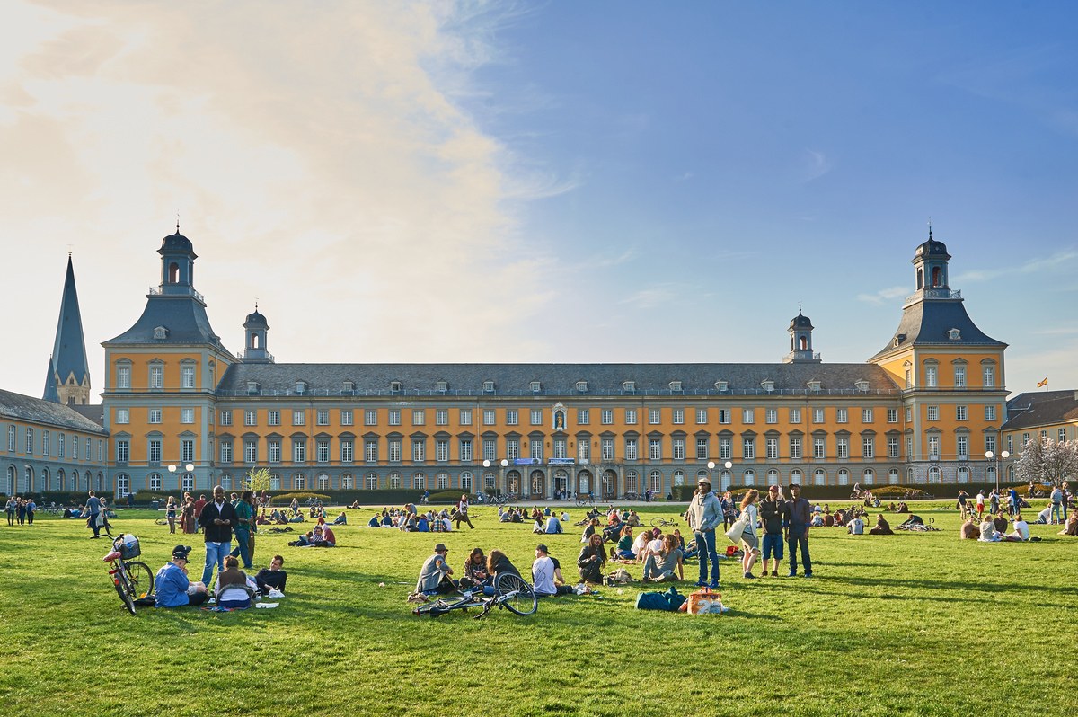 Eine Wissenschaftlerin und ein Wissenschaftler arbeiten hinter einer Glasfassade und mischen Chemikalien mit Großgeräten.